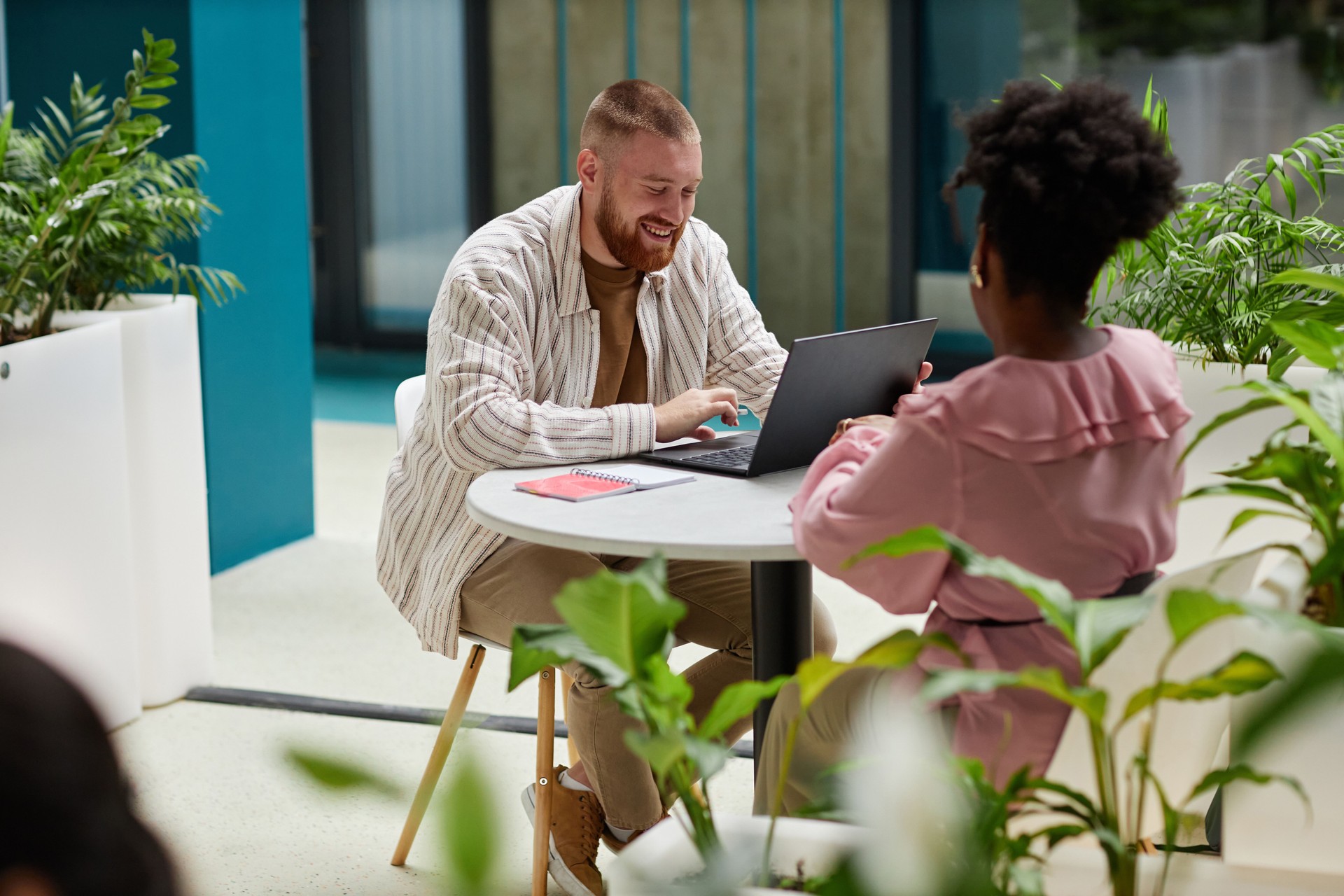 Smiling Man Using Laptop Sitting at Table with Female Colleague in Office Center